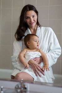 Mother in a bathrobe and with a child standing in the bathroom