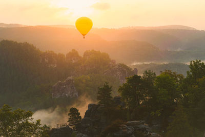 Hot air balloon flying over trees against sky during sunset