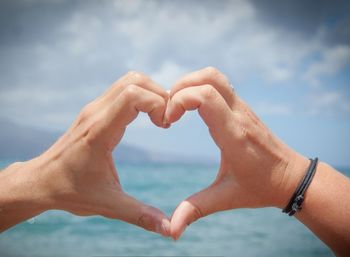 Cropped image of hands making heart shape against sea