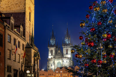 Low angle view of decorated christmas tree and tyn church against blue sky at night