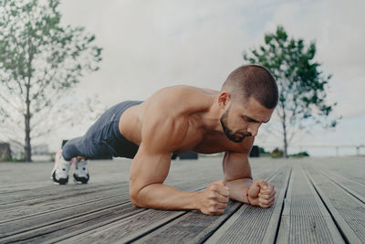 Shirtless young man exercising on footpath