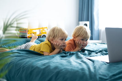 Cute kids looking at laptop lying on bed