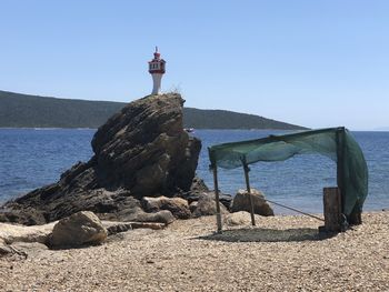 Lighthouse on rocks by sea against clear sky