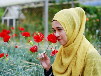 Woman smelling red flower blooming on field