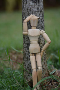 A wooden mannequin leaning on the tree trunk 