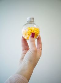 Cropped hand holding candies in glass against white background