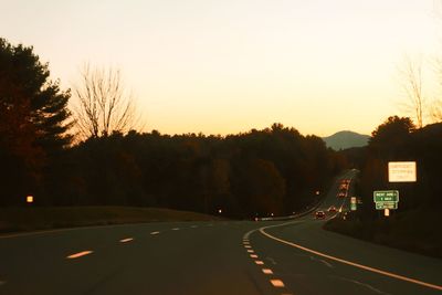 Road by silhouette trees against sky at sunset