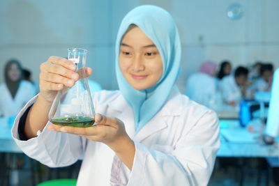 Woman wearing hijab holding flask at laboratory