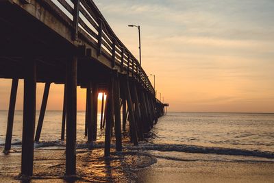 Silhouette pier on beach against sky during sunset