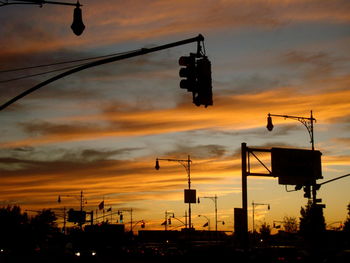 Silhouette road signal and street light against sky during sunset