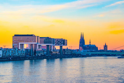 View of river by buildings against sky during sunset