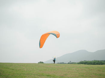 Person paragliding on field against sky