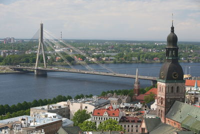 Buildings by bridge and river against sky on sunny day