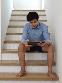 Full length of young man holding digital tablet sitting on staircase