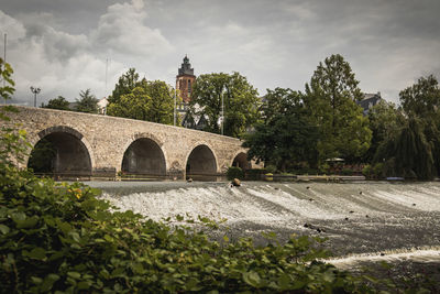 Arch bridge over river by building against sky