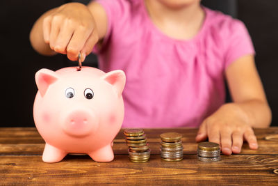 Midsection of girl inserting coin in piggy bank on table