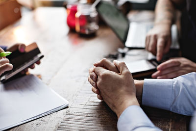 Cropped image of business people using mobile phone and doing paperwork at table in restaurant