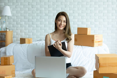 Portrait of woman using laptop while sitting amidst cardboard boxes at home