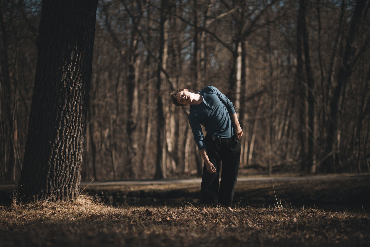 tree, one person, real people, plant, tree trunk, trunk, land, forest, lifestyles, nature, leisure activity, standing, field, casual clothing, day, woodland, full length, outdoors, bare tree, human arm
