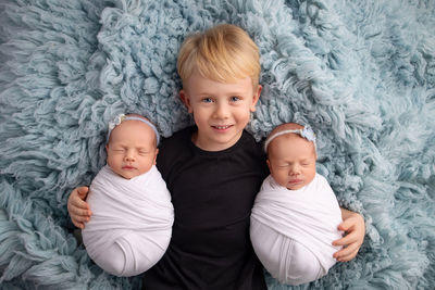 Directly above shot of brother with babies lying on bed