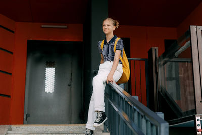 A teenage girl laughs and slides down the railing on her way to school. a cheerful girl hurries 