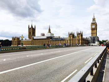 Road passing through city against cloudy sky