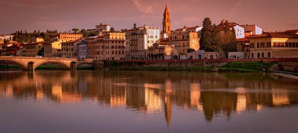 River by buildings against sky during sunset