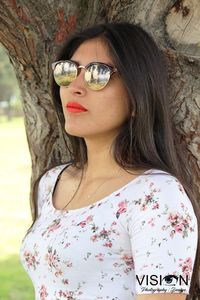 Close-up portrait of young woman standing against tree trunk