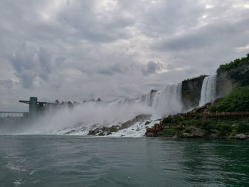 Scenic view of waterfall against cloudy sky