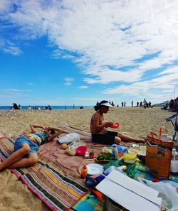 People sitting on beach by sea against sky