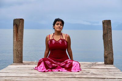 Portrait of woman sitting on pier against sky