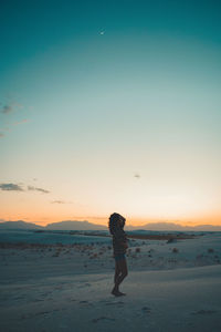 Woman standing on beach against sky during sunset