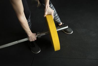 Low section of woman adjusting weight on barbell while exercising in gym