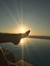 Woman hand by lake against sky during sunset