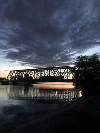 Silhouette bridge over river against sky at sunset