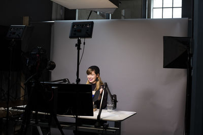 Smiling female entrepreneur explaining about product while broadcasting through television camera at office