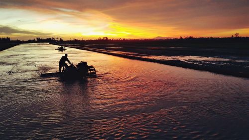 Silhouette people on river against sky during sunset