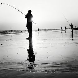 Silhouette man fishing at beach against sky