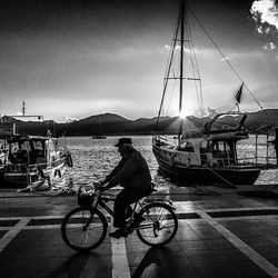 Man riding bicycle on harbor against sky