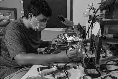 Black and white photo of a repairman using a hot soldering iron to fix a computer motherboard.