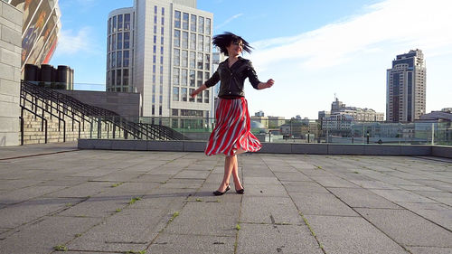 Happy woman wearing striped skirt and jacket on footpath in city