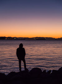 Silhouette man looking at sea against sky during sunset