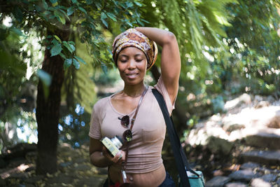 Smiling young woman standing against trees in forest