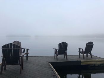 Empty chairs on pier over lake against sky