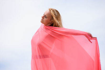 Young caucasian woman standing in desert against blue sky, covered with pink fabric.