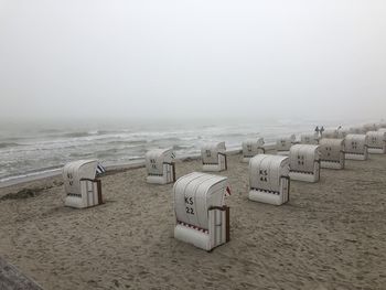 Hooded chairs on beach against sky