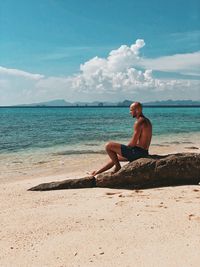 Full length of shirtless man sitting on beach