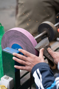 Master sharpens ax on electric sharpener with bright sparks and holds blade with his brutish fingers