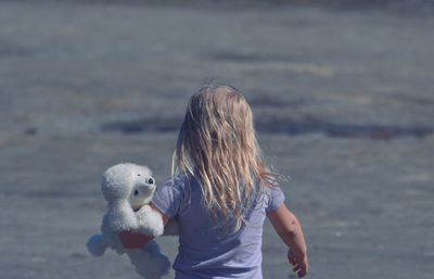 Rear view of girl with stuffed toy walking at beach