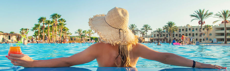 Rear view of woman holding cocktail glass in swimming pool